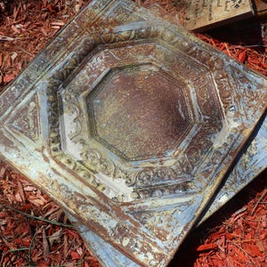 Puede incluir: Dos tejas de techo cuadradas de metal superpuestas con un diseño octogonal decorativo. Las tejas son una mezcla de azul, verde y marrón con una pátina oxidada.