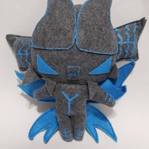 Peut inclure: Un jouet en peluche gris en feutre avec des ailes bleues et un motif en forme de Y au dos. Le jouet a une grosse tête avec deux grandes oreilles triangulaires et une petite bouche carrée.