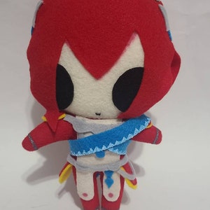 May include: A handmade plush toy of a character with red hair, a white face, and a blue and gray outfit. The toy is standing on a white surface.