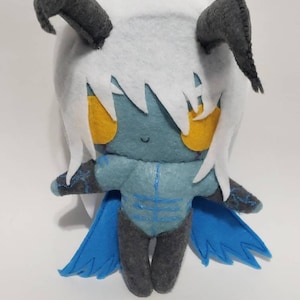 May include: A plush toy with blue wings, gray horns, and a white fluffy head. The toy has a blue and gray body with yellow eyes and a small smile.