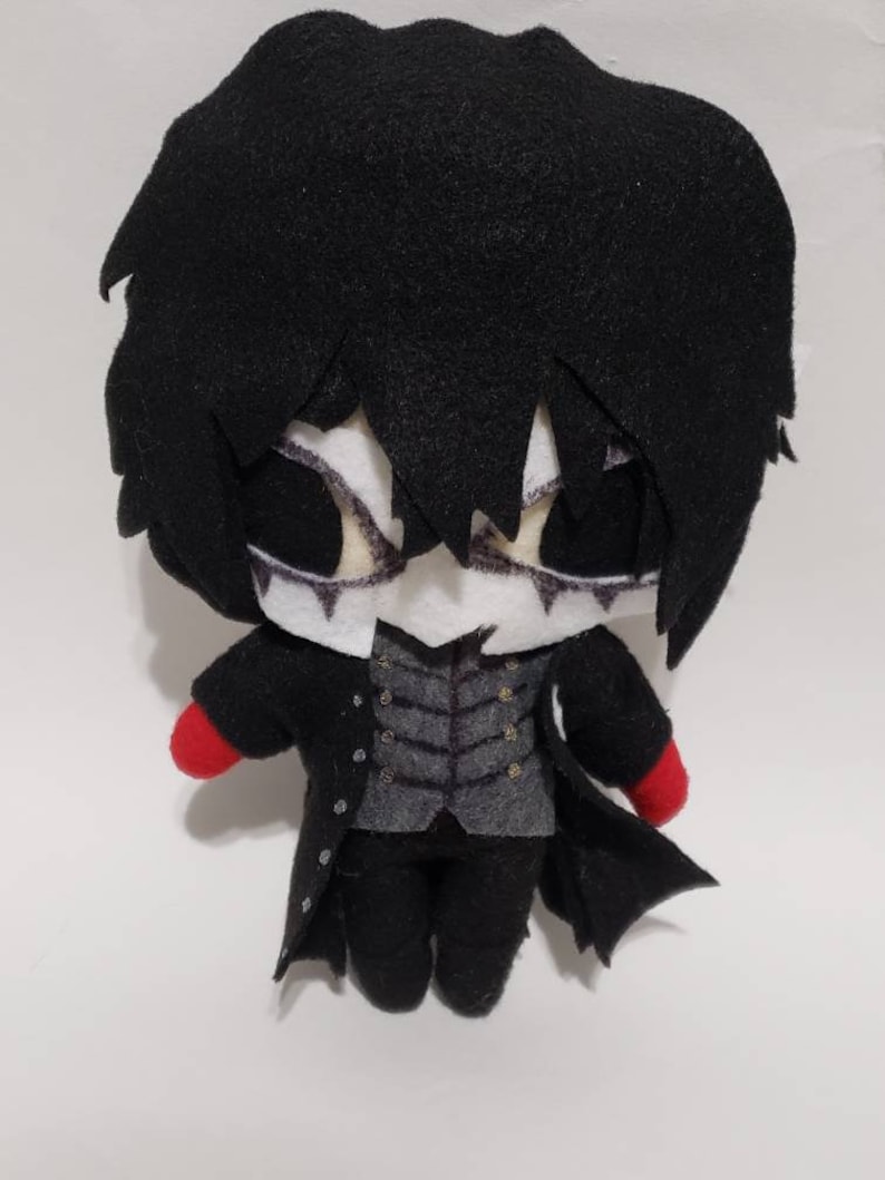 May include: A black and red plush toy of a character with black hair, a black coat, and a white face. The toy has a small, round body and large eyes.