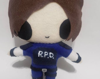 May include: A plush toy of a character from the Resident Evil video game series. The toy is wearing a blue uniform with the letters "R.P.D." on the chest. The toy has brown hair and a white face with black eyes.