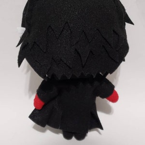 May include: Black and red plush toy of a character with spiky black hair and a black coat. The toy is facing away from the camera.