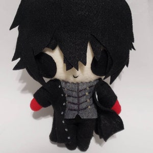 May include: A black and white plush toy of a character with black hair, a black coat, and red gloves. The toy has a simple, cartoonish style.