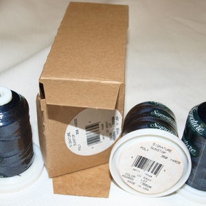 May include: Three spools of dark blue thread with white labels that read "Signature Sunstop Poly 360 Yards". The spools are sitting on a white surface next to a brown cardboard box.