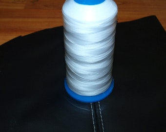 May include: A spool of white thread with a blue plastic top and bottom, sitting on a black surface.