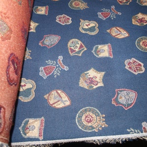 May include: Blue fabric with a repeating pattern of colorful crests and shields. The fabric has a fringed edge.