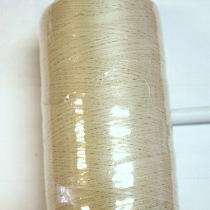 May include: A spool of off-white thread wrapped in clear plastic with a blue plastic cap.