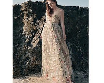 Puede incluir: Vestido largo beige con tirantes finos, adornado con bordados florales en tonos rojos, rosas y verdes. La tela transparente crea una silueta fluida. Ideal para una ocasión especial.