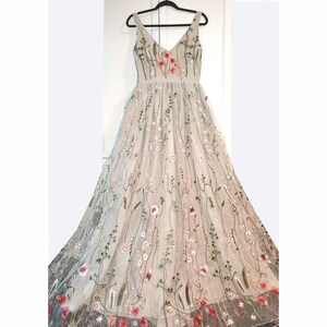 May include: A long, flowy, beige tulle dress with a V-neckline and delicate floral embroidery in shades of pink, red, and green.