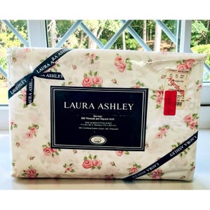 May include: A Laura Ashley queen fitted sheet in a cream color with a pink rose floral pattern. The packaging features a black label with white text stating 200 threads per square inch, 60 by 80 inches, and 50 percent combed cotton and polyester.