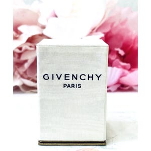 May include: A rectangular, off-white, textured fabric box featuring the black text GIVENCHY PARIS printed on the front. The box has a clean, structured design with a dark base, presenting a minimalist appearance for a product container.