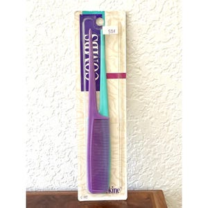 May include: A purple comb with a pointed handle and fine teeth, packaged on a teal and white card. The card reads "Combs" in white text and has a price tag. The comb is a hair care accessory.