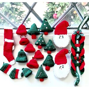 May include: A collection of handmade crochet Christmas ornaments. The assortment includes red and green Christmas trees, Santa faces, bells, stockings, and a garland. The ornaments are displayed against a window with a blurred background.