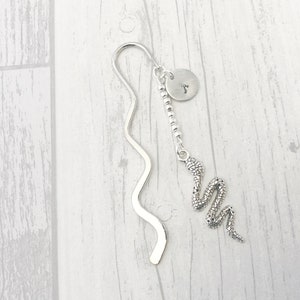 May include: Silver bookmark with a snake charm and a personalized disc. The bookmark is wavy and has a beaded chain.