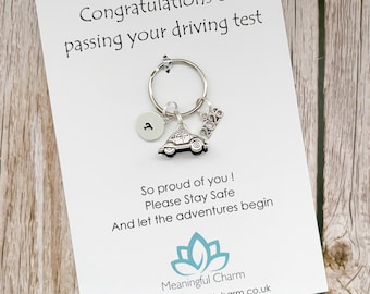 Puede incluir: Un llavero de tono plateado con un dije de coche pequeño, un disco circular con la letra T y un dije de 2026. El llavero está sujeto a una tarjeta blanca impresa con el texto Congratulations on passing your driving test, So proud of you, Please Stay Safe, And let the adventures begin y el logotipo de Meaningful Charm.