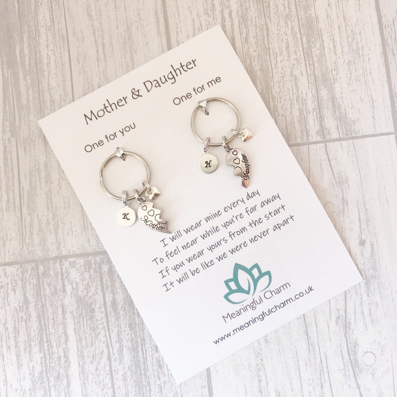 May include: Two silver keychains with charms that say "Mother" and "Daughter". The keychains are attached to a card with a poem that reads, "I will wear mine every day To feel near while you're far away If you wear yours from the start It will be like we were never apart".