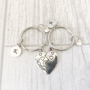 May include: Two silver keychains with a heart charm that says "Mother" and "Daughter" on each half. The keychains have initial charms that say "K" and "H".