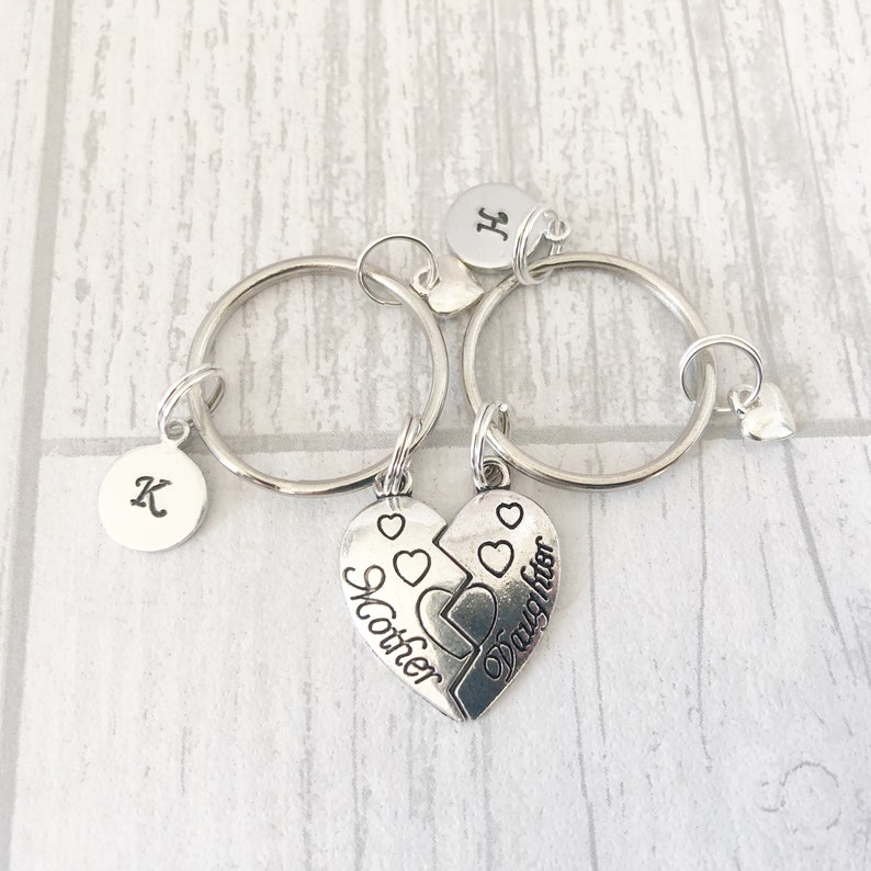 May include: Two silver keychains with a heart charm that says "Mother" and "Daughter" on each half. The keychains have initial charms that say "K" and "H".