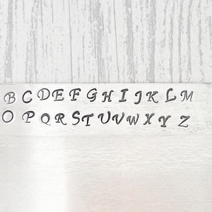 May include: A metal plate with the alphabet in cursive lettering. The letters are arranged in two rows, with the first row being A through M and the second row being N through Z.