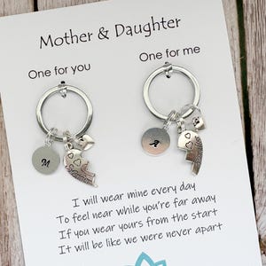 May include: Two silver-toned keychains attached to a white display card labeled Mother & Daughter. Each keychain features a circular ring, a small round charm with a letter, a heart-shaped charm, and a puzzle-piece heart charm engraved with Daughter.