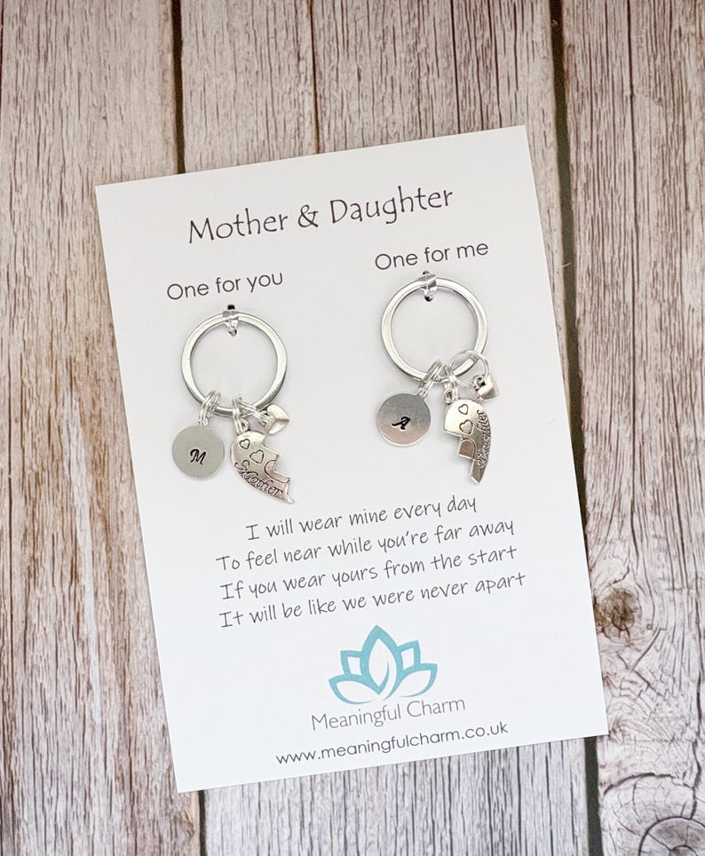 May include: Two silver-toned keychains attached to a white display card labeled Mother & Daughter. Each keychain features a circular ring, a small round disc with a letter, a heart charm, and a puzzle-piece charm engraved with the word Mother or Daughter.