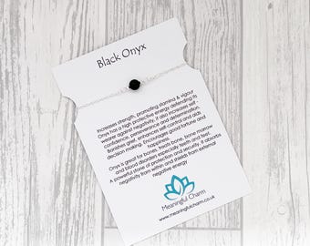 May include: A delicate silver chain bracelet featuring a single round black onyx bead, displayed on a white card with the text Black Onyx and a detailed description of the stone's properties, along with the Meaningful Charm logo and website.