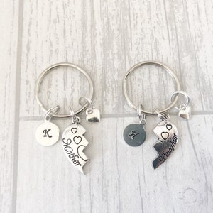 May include: Two silver keychains with split heart charms. One charm says "Mother" and the other says "Daughter". Each keychain also has a small heart charm and a round charm with a letter.