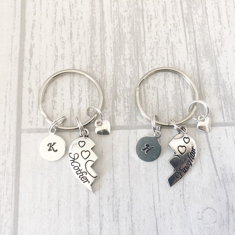 May include: Two silver keychains with split heart charms. One charm says "Mother" and the other says "Daughter". Each keychain also has a small heart charm and a round charm with a letter.