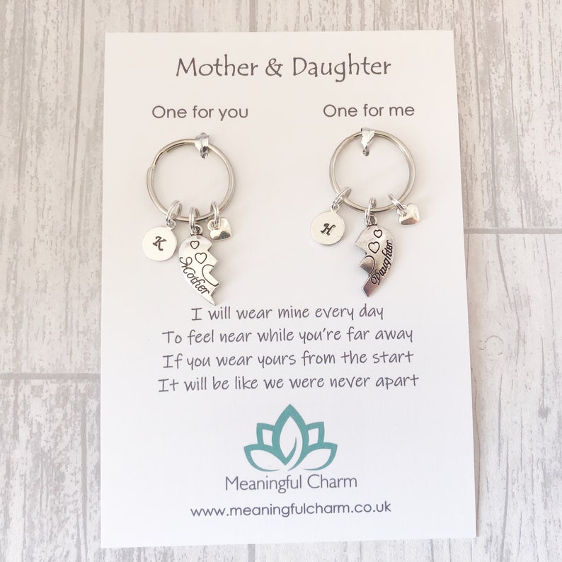 May include: A set of two silver keychains with a broken heart charm that says "Mother" and "Daughter". The keychains are on a white card with the text "I will wear mine every day to feel near while you're far away. If you wear yours from the start it will be like we were never apart." and the logo "Meaningful Charm" with the website address "www.meaningfulcharm.co.uk".