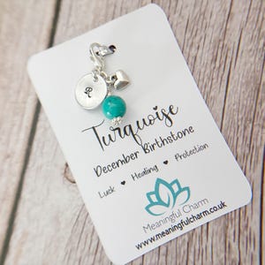May include: A silver-toned charm featuring a round disc stamped with the letter R, a small heart, and a round turquoise bead. The charm is attached to a white display card printed with the text Turquoise December Birthstone, Luck, Healing, Protection, and Meaningful Charm.