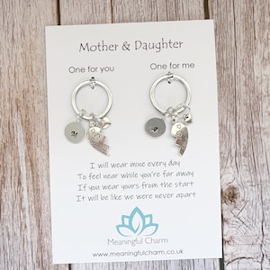 May include: Two silver-toned keychains on a white display card labeled Mother & Daughter. Each keychain features a circular ring, a small round disc with a letter, a heart-shaped charm, and a puzzle piece charm engraved with the word Mother or Daughter.