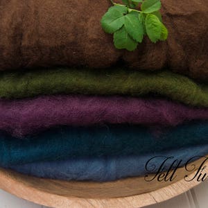 May include: Four different colors of wool roving stacked on top of each other in a wooden bowl. The colors are brown, green, purple, and blue.