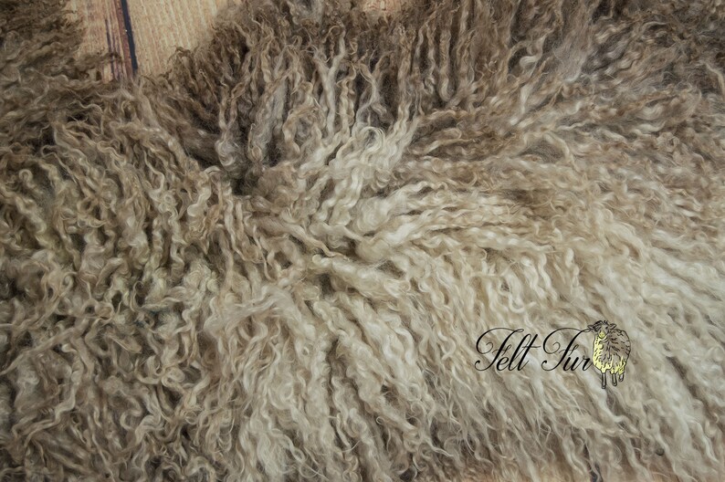 May include: Close-up of a sheepskin pelt with a dense, curly texture. The wool is a mix of light and dark brown tones, creating a natural, textured appearance. The words "Felt Fur" are visible in the lower right corner.