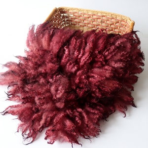 May include: A deep burgundy fluffy newborn photography prop made of faux fur. The prop is in a woven basket.
