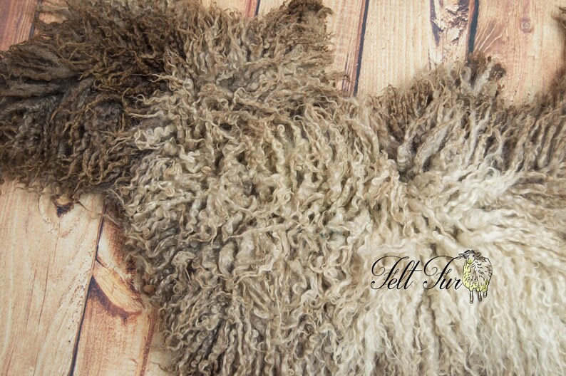 May include: A close-up of a sheepskin pelt with a curly, textured appearance. The pelt features a mix of brown, tan, and cream colors. The image is taken on a light brown wooden surface. The text "Felt Fur" is visible in the image.