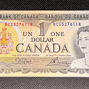 May include: A Canadian one-dollar banknote with a portrait of a woman and the text "ONE DOLLAR CANADA". The bill includes the text "BANK OF CANADA" and "BANQUE DU CANADA". The serial number BCG5276118 is printed on the bill.