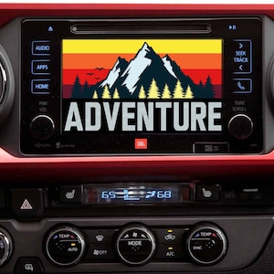 May include: A car dashboard with a screen displaying a mountain range graphic and the word "ADVENTURE". The screen is part of a car stereo system with buttons for audio, apps, home, power, and volume.