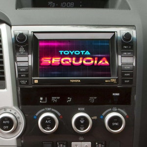May include: A black dashboard with a touchscreen display showing the text "TOYOTA SEQUOIA" in a retro-style font. The display is surrounded by buttons for controlling the radio, climate, and other vehicle functions.