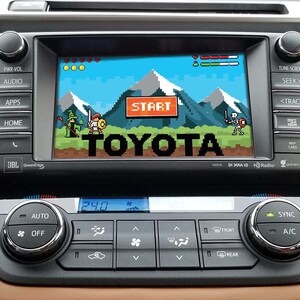May include: A car dashboard with a screen displaying a pixelated video game. The game features a character in a green tunic and a character in blue armor. The screen also displays the word "START" and the word "TOYOTA".