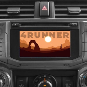 Puede incluir: Un tablero de automóvil con una pantalla que muestra el texto "4RUNNER" y un paisaje de puesta de sol con una formación rocosa. La pantalla está rodeada de botones etiquetados como "Audio", "Apps", "Home", "Power Vol", "Tune Scroll", "Seek", "Track" y "Radio".