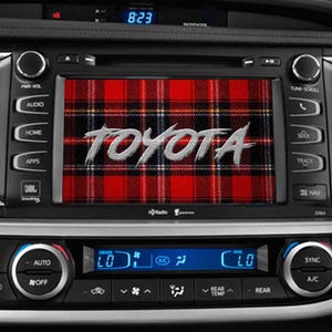 May include: Close-up of a car's dashboard with a digital display showing the time. The infotainment screen displays the word "TOYOTA" over a red and black plaid pattern. Various buttons and controls are visible.