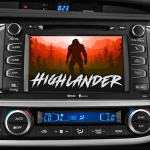 May include: A car dashboard with a screen displaying a red and orange image of a large, dark silhouette of a creature in a forest. The text "HIGHLANDER" is displayed on the screen in white letters. The time 8:23 is displayed on the top of the screen.