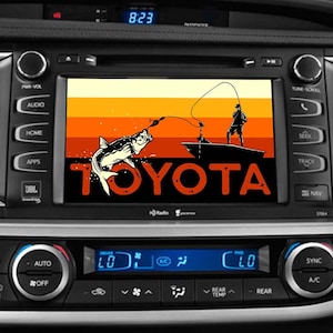 May include: A black and orange graphic on a car's dashboard screen shows a silhouette of a person fishing from a boat with a fish jumping out of the water. The text "TOYOTA" is in red letters below the graphic.