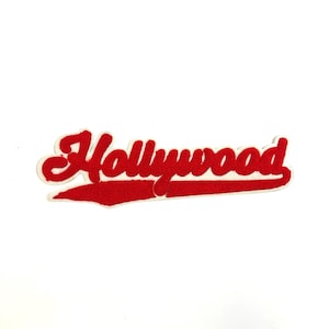 May include: A red and white embroidered patch with the word "Hollywood" in a script font. The word is in red with a white outline, and the patch has a white background.
