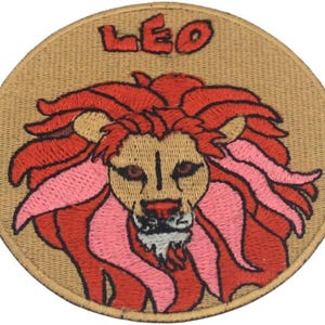 May include: Embroidered patch featuring a lion's head with a red mane and pink accents, set against a tan background. The word "LEO" is embroidered in red at the top. This patch is likely a zodiac sign emblem.