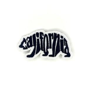 May include: A navy blue patch in the shape of a bear with the word "California" spelled out within the bear's silhouette. The patch has a white border and is likely an iron-on or sew-on emblem.