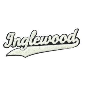 May include: A white and black embroidered patch with the word "Inglewood" in a script font. The text is in white with a black outline and sits on a white banner. The patch has a textured, fuzzy appearance.