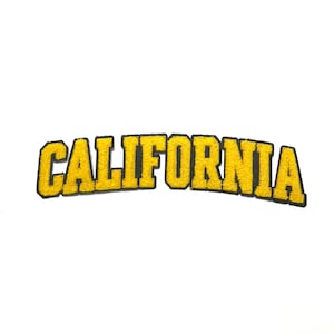 May include: A yellow felt patch with the word "CALIFORNIA" in a bold, arched font. The letters are outlined in black, creating a contrasting border. The patch is likely for clothing or accessories.