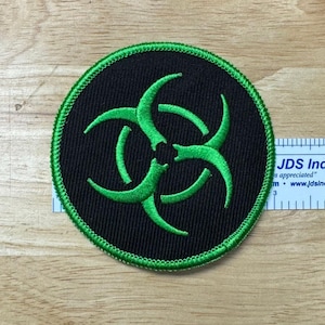 May include: Green biohazard symbol embroidered on a black circular patch with a green border.